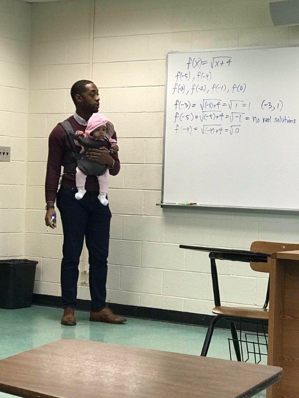 A student had to bring his kid to class. The professor held the girl for him.