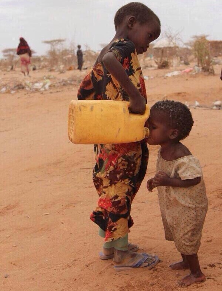 Girl offers water to her little sister.