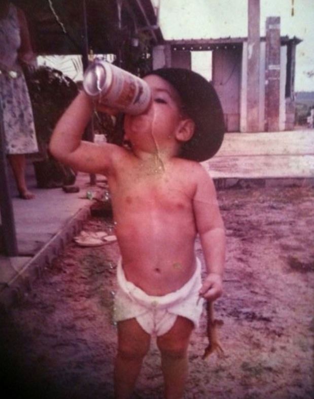 Vintage photo of a very small child in a diaper drinking what looks like a beer