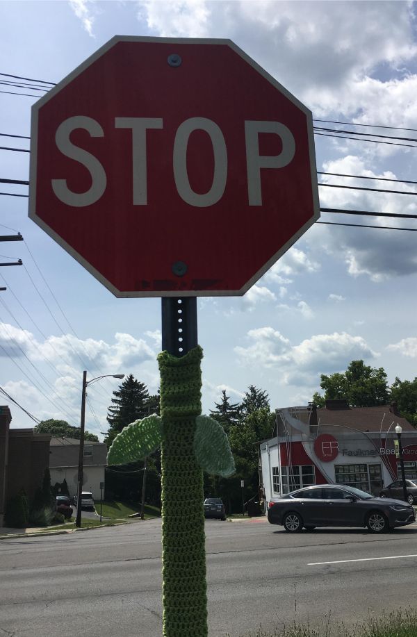 Someone knitted a stem and leaves on this stop sign.