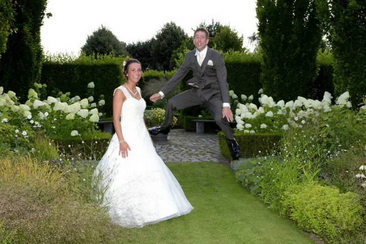 Man that looks like he's hovering while jumping next to his wife during a perfectly timed wedding photo