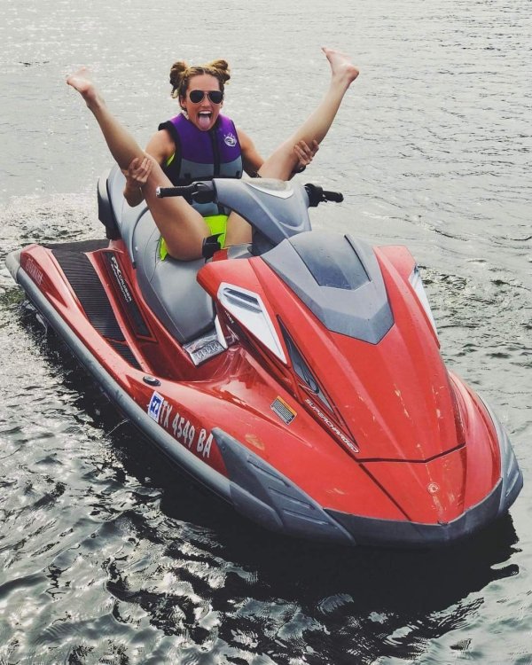 Woman sticking her tongue out and pulling her legs back while on the back of a jet ski