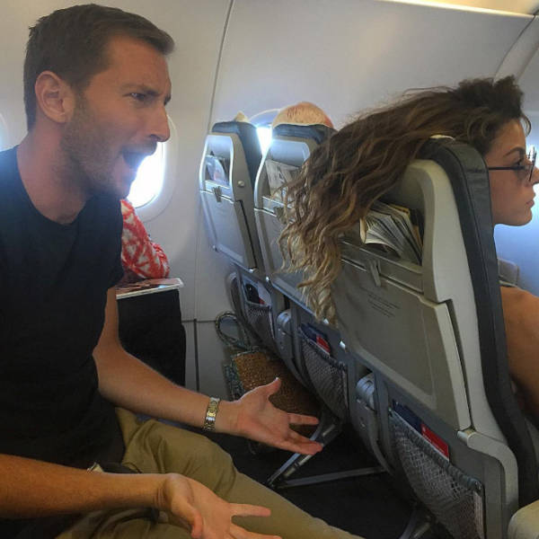 Guy looking in horror as womans hair hangs over the back of her airplane seat covering his tv