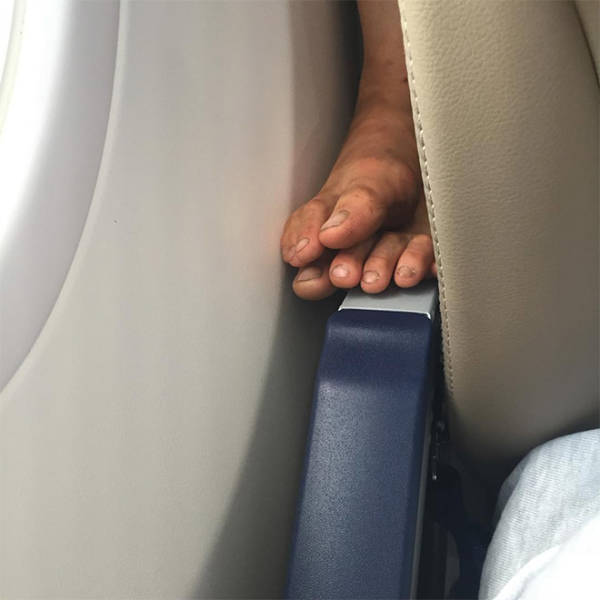 Disgusting dirty feet on the armrest of a seat on an airplane