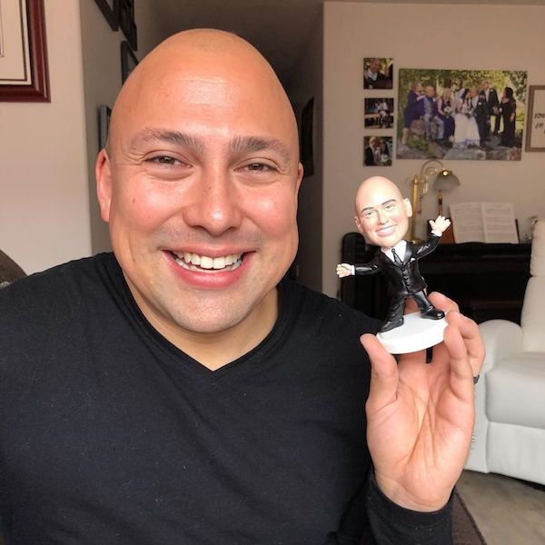 guy smiling next to his personalized bobble head doll