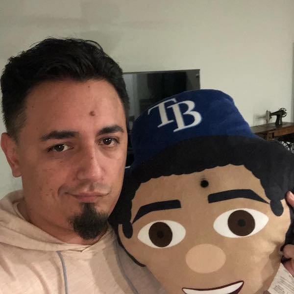 guy holding big stuffed doll that looks like him with mole on forehead