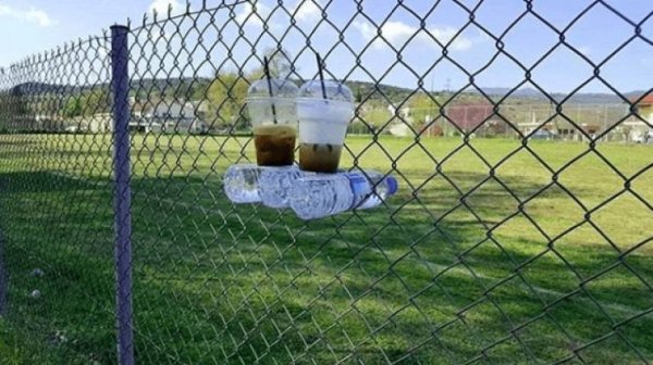 water bottles stuck in a fence to act as little table for iced coffees
