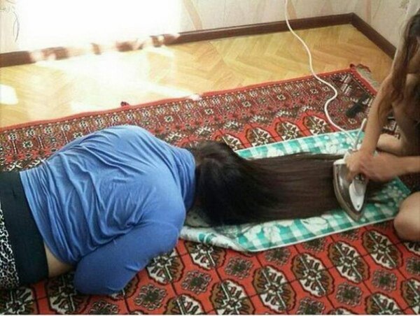 woman getting her hair straightened on the floor by a clothes iron