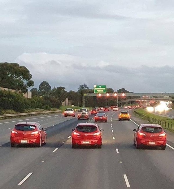 3 identical red cars line up adjacently on a highway