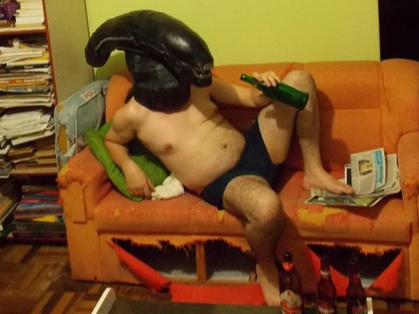guy wearing alien mask with no clothes on drinking beer on the couch