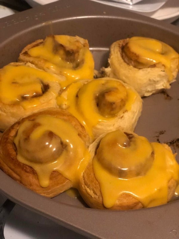 cinnamon rolls with orange icing but one roll has melted nacho cheese on it