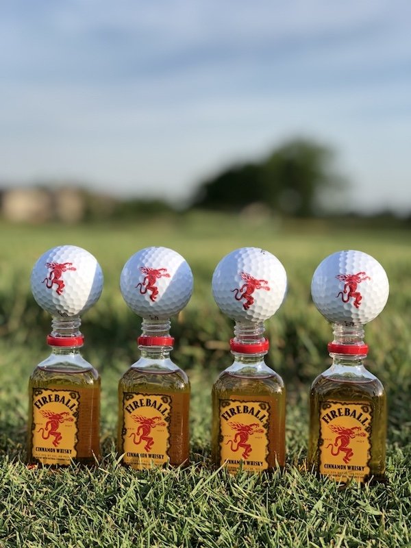golf balls teed up on tiny whisky bottles