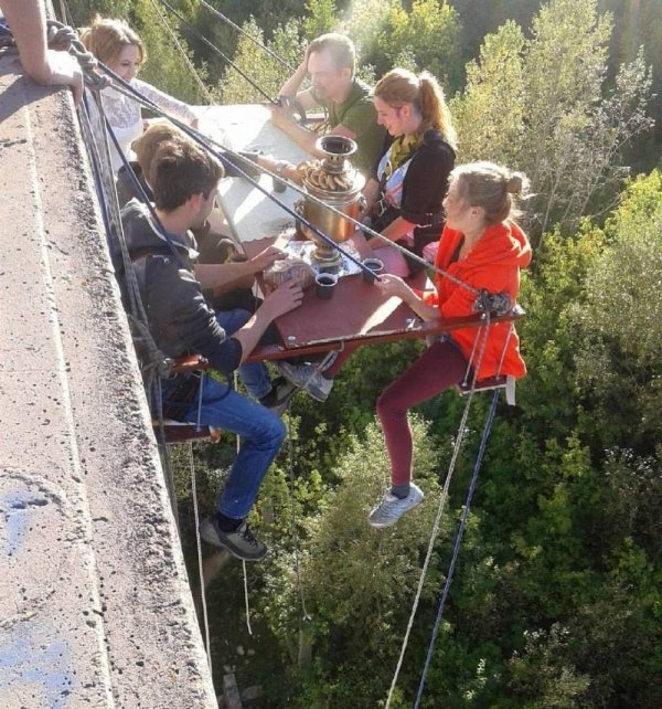 people hanging off the side of a cliff eating lunch