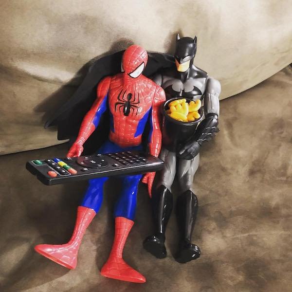 action figures spider-man batman holding the TV remote