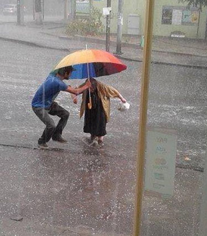 feel good pics - guy trying to protect old woman from the rain