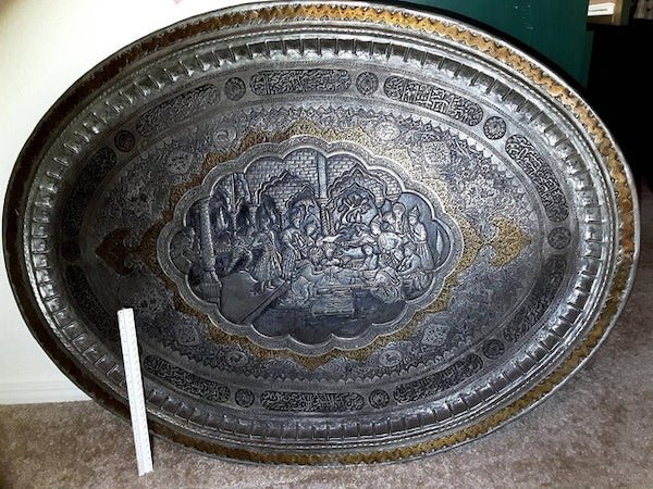 Massive intricate platter purchased by my grandfather in Saudi Arabia in the 60’s. 1 ft ruler for scale. Islamic calligraphy, scene depicting an old story maybe?

A: It’s a table. You’re missing the bottom. I’ve seen them sold as wall hanging often. I’ve got one. Mine doesn’t have a picture its covered in flowers. I’m sure they have a name but haven’t been able to find it. Search Turkish brass coffee table….. that’s the closest to finding a name I’ve come.