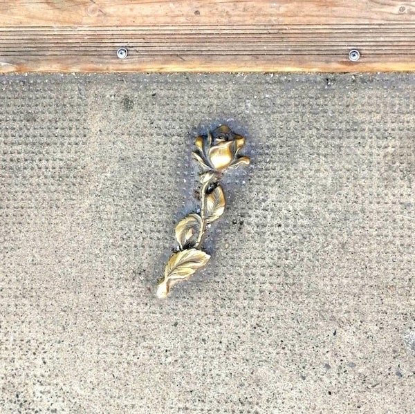 curious objects - gold metal rose attached to the sidewalk