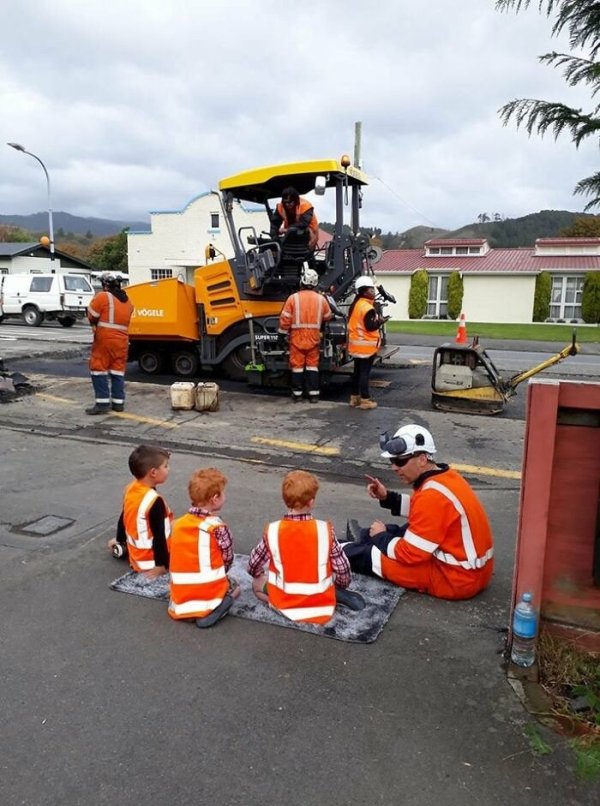 children sitting with worker on road construction