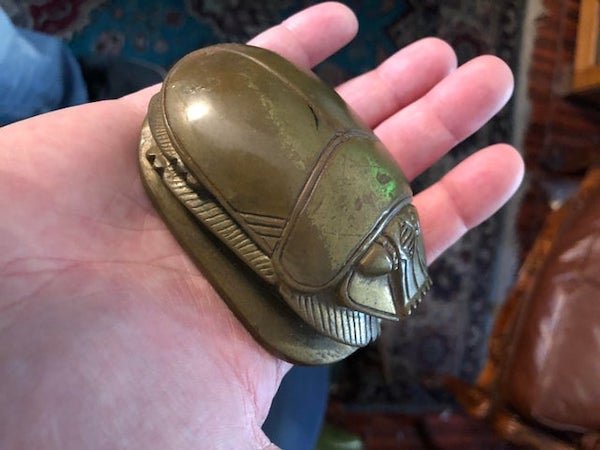 Solid metal Egyptian-looking scarab. My gma believes she got it somewhere in Europe a long time ago. It has hieroglyphs on the underside and is fairly heavy for its size.

A: Likely a paper weight. Did a quick google for “scarab paperweight” and found a lot of similar items.