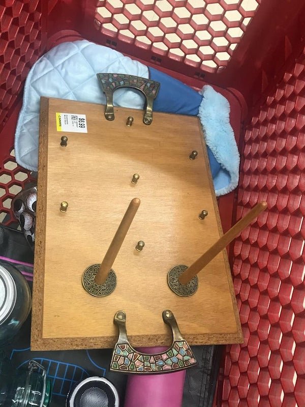 A friend found this tray at a thrift store. It has ornate inlay handles and brass knobs in two sizes. No markings on the bottom and all searches come up empty. What is this thing?

A: It’s a bagel tray. The button pegs would have kept glass dishes in place