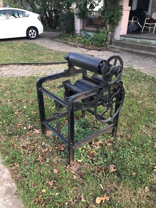 Some type of old pressing machinery in my friend’s neighbor’s yard

A: I’m leaning towards older printing press. For lino cuts, wood block, or even paper-making, you’ll run it through a press. It obviously helps put ink on paper, but it will also press out water from the paper being made. If I’m right, it would be missing a flat surface to put stuff on as it goes through the rollers.