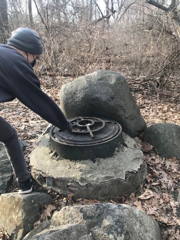 This structure I found while walking in the woods, the metal bit is about 2 feet wide and looks like it could uncomfortably fit a person in it. My guesses are a well, sewer or time capsule. For context I live in eastern Massachusetts. We plan on going back to open it

A: Definitely a man hole. Do not open it. DEFINITELY DO NOT GO IN IT! Manholes are notoriously deadly because they contain low oxygen percentages and high concentrations of poisonous gases such as hydrogen sulfide and methane. First responders usually find two dead people in manholes – the first one that went in and succumbed and their friend who watched them pass out and rushes in to help.