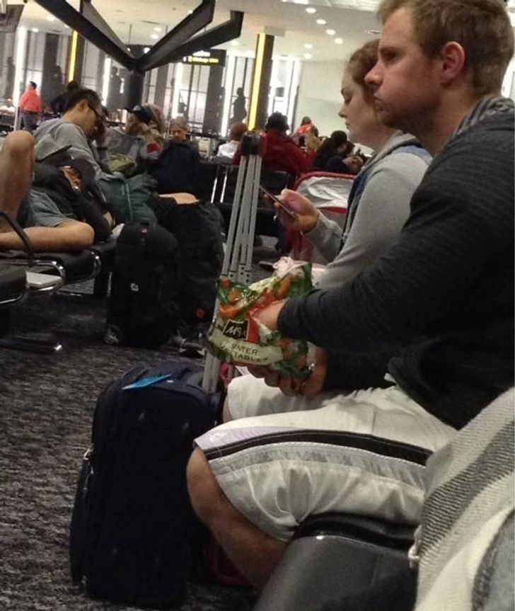 funny airport pics - man eating bag of frozen vegetables waiting at the airport