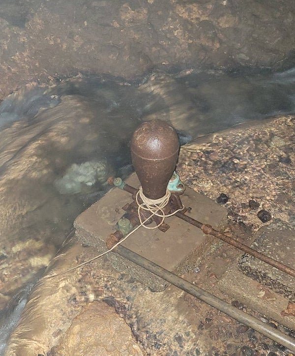 Found 100 feet underground in old cave/mine. It’s rusted metal, about 2 feet tall with pipes attached. The white thing is electrical wire wrapped around it.

A: Hydraulic ram