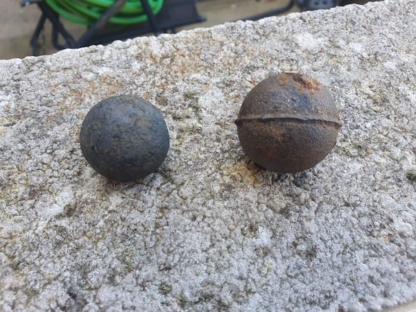 Two iron(?) balls pulled out of a river in the UK. They are solid and magnetic. The larger one retains its casting seam.

A: Balls for a ball mill. The one that shows the casting you can see where they sliced the sprue off.