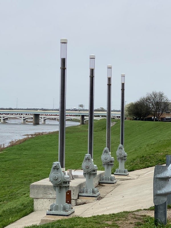 Tubes along the river right next to a water inlet and/or outlet, are they for measuring water level or something?

A: It’s the stem that rises and lowers as the gate goes up and down. They work like a screw with a handle or motor operator. These appear to be fully open. I worked in water/waste water 20 yrs.