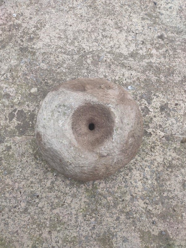 Found this buried. It’s flat on one side, concaved on the other and has a hole right through the middleA: This is likely to be a prehistoric or Roman quernstone. This would be the top, a spindle would connect it to a bottom piece and grain would be poured into the ‘funnel’ on top and ground between the two stones to make flour.