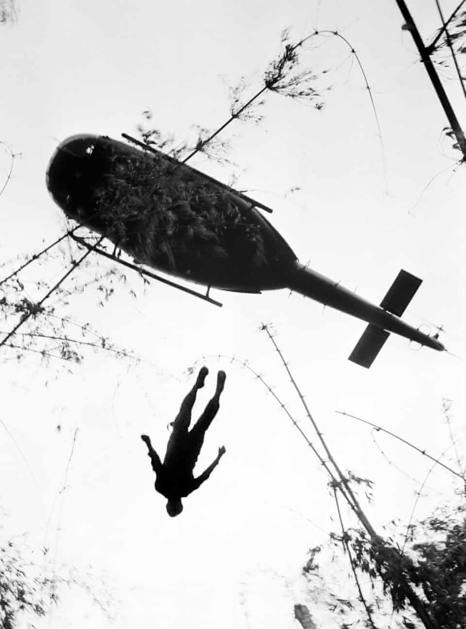 The body of a US paratrooper killed in action in the jungle near the Cambodian border is lifted up to an evacuation helicopter in war zone C, 14 May 1966, during the Vietnam War