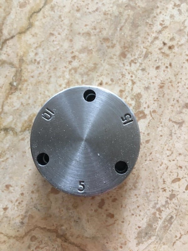 Circular metal disk with numbers 5, 10, 15 on one side. Found in a kitchen.

A: It goes with a pressure cooker. The lid has a small, pointed opening and that sets on top of it. The lid locks onto the pot and that regulates the pressure inside.