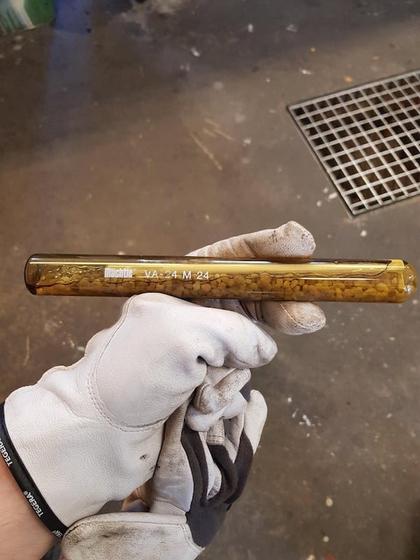 Customer came in with this at work. Seems to be 2 or 3 different compounds all encased in unopenable glass.

A: This is an epoxy capsule used to glue a threaded stud into concrete. A hole of appropriate size (25mm in your case) to a specified depth.. he capsule is put in the hole and the stud is used to break , mash and mix the two part epoxy adhesive in the hole .. the other granules are to roughen the hole and aid in the mixing.