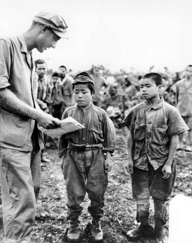 Marine First Lieutenant Hart H. Spiegal of Topeka, Kansas, uses sign language as he tries to strike up a conversation with two tiny Japanese soldiers captured on Okinawa. The boy on the left claims he is “18” while his companion boasts “20” years. 1945