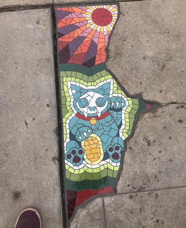 This crack in the pavement is filled with a stained-glass cat portrait.