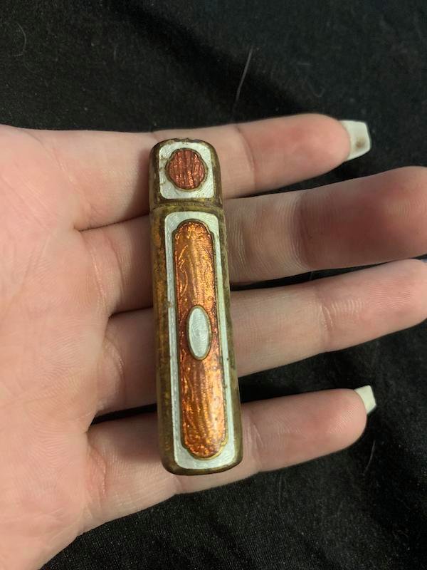 2 inch long metal thing, top piece slides out, there is a slit in the back side of the top piece when taken apart. Cylindrical but not exactly round, more oval shaped.

A: I am sure it’s some kind of antique lipstick tube.