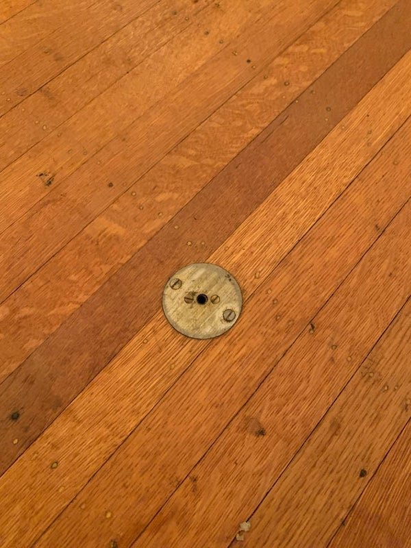 Small metal hole in the center of dining room floor of a home build in 1920. Below it in the basement, two wires come out but have since long been cut and don’t show what they went to.

A: Fancy houses would have little foot-actuated buttons under the dining table to call for the help, given the location in the center of the dining room and the wiring.