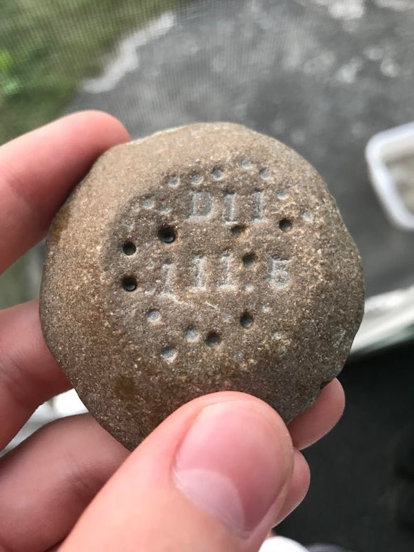 Found this stone on a beach in northern LP Michigan, it’s about 2 inches across and is strangely light for its size. The holes on top look man made, along with what I assume to be the characters D11 111.5

A: Not ballast, they used regular round stone for that. Based on the area you found it, petobego pond area was a large Marl clay quarry for the Elk Rapids Portland cement co. My best educated guess is it was a processed and fired piece of marl clay as a quality test. Hence the markings for a batch number. I am on board of that region’s underwater preserve council and trained underwater archeologist….. suggest you take to Elk Rapids historical museum for confirmation. Very nice and knowledgeable folks there.