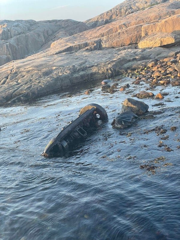 Large object revealed in low waters on an island in southern Sweden. Around 3m long, looks to be made of metal with mechanical components, except for a round stone at the end.

A: Skandia hot-bulb engine.