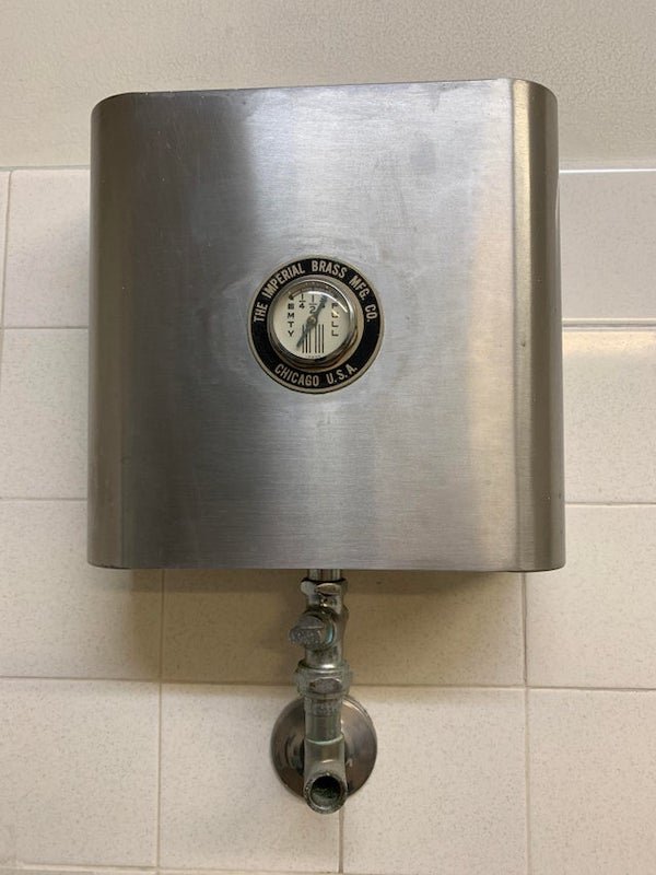 Gauge on a tank, found in a bathroom above the sinks

A: Tank feeding a central liquid soap dispensing system. Was common in American government buildings.