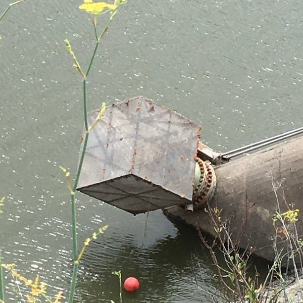 Large, cube shaped object attached to some sort of duct near a dam. Would normally be under the reservoir water; seems to be made of a translucent material?

A: It’s a strainer for the water intake.