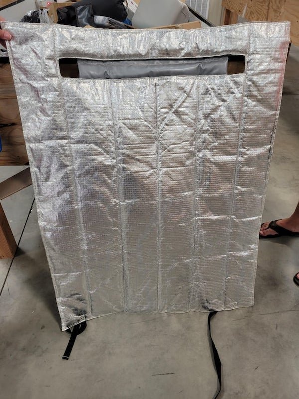 Some type of reflective blanket maybe? Insulation? Debris from a re-entry capsule? Weird therapy thing? Appx 3 foot wide, by maybe 4 tall. Has some ‘bulk’ but not much – maybe 5 pounds. Back side is grey vinyl. Found in a “Bargain Bins” place, but cant match with anything on Amazon…

A: Hey, I know this one! It’s a grill blanket. It’s for more of a smoker/barrel shaped grill (Traeger is a popular brand). The handle of the grill lid fits into that slot and the straps come around to the front to fully wrap around the grill body. Conserves heat a lot better, especially in the colder months.