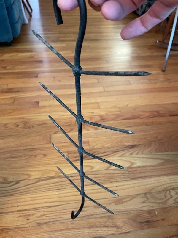 Metal, a couple of feet long, with hooks on either end (offset 90°), with nail-like spikes down either side.

A: I’ve seen these used for drying corn for seed. Place an ear on each spike and hang it to dry.