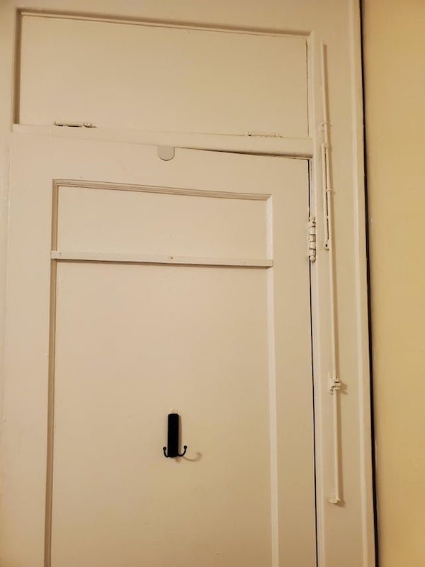 Metal bar to the right of the door in a old apartment building built in 1926.

A: It was used to open and close the transom window above the door.