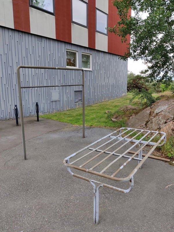 Those metal structures, found near buildings in residential areas in Sweden. They are all slightly different, and I didn’t see them used by anyone.

A: The upright one is for hanging a carpet on and wacking it with something to get dust off. The table like one I assume it’s for drying a carpet or towels or similar.