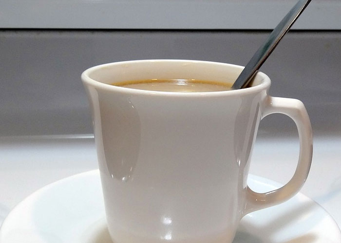 Overstirring coffee with a metal spoon in a ceramic coffee mug.