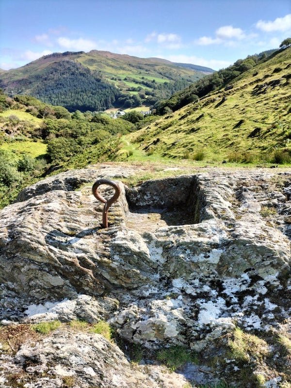 What is this hoop and square block cut out of the stone? In the middle of nowhere in Wales, UK

A: This could be a mounting location for raising a boundary marker, flag pole, statue, cross… heck even a fountain or an animal feeding station.