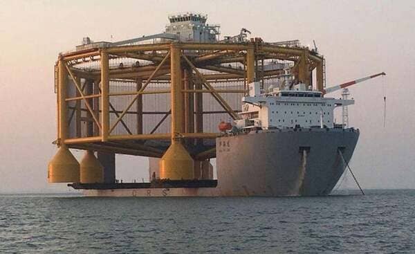 A new offshore fish farm during transport to Norway. Humans can be seen on the deck of the ship. The farm is 110m wide, 68m high, contains 250 000 cubic meters in volume and can mature up to 1.5 million fish in just 14 months.