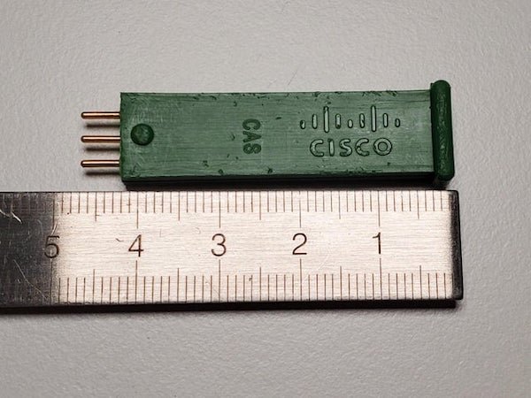 Green rectangular key with 3 pins on one end and CISCO, CAS, and a ‘0’ printed on it.

A: This is a cable access system pad. It’s used in the silver / green cable distribution amplifiers (nodes) to modulate the signal out. The 0 indicates it removed no signal and allowed full power out down the run.